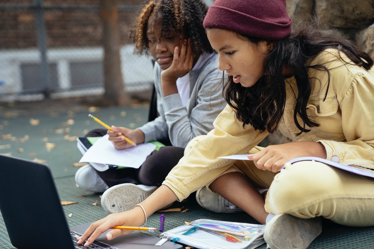 Two schoolgirls study outdoors.