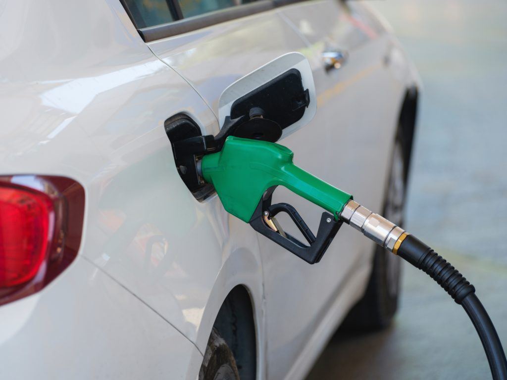 Green gas pump nozzle in the fuel tank of a white car