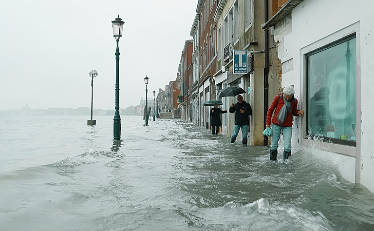 People struggle along a narrow footpath in Venice, up to mid calf in moving water, the morning after the 2019 flood disaster.