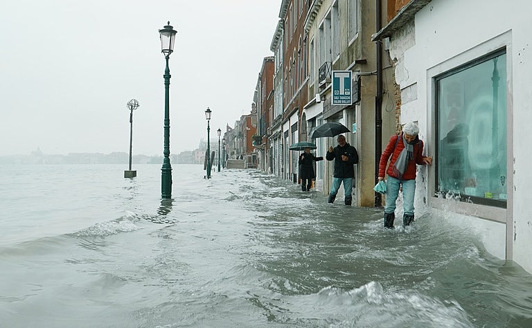 People struggle along a narrow footpath in Venice, up to mid calf in moving water, the morning after the 2019 flood disaster.