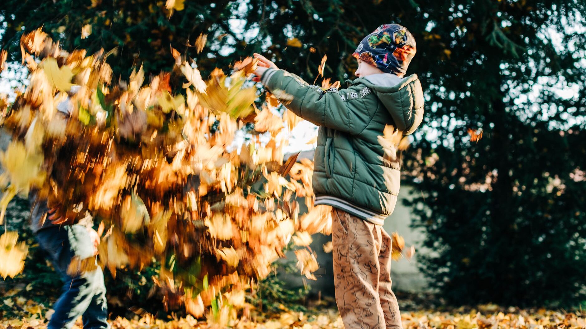 Two children joyfully playing with leaves in a sunlit autumn park setting.